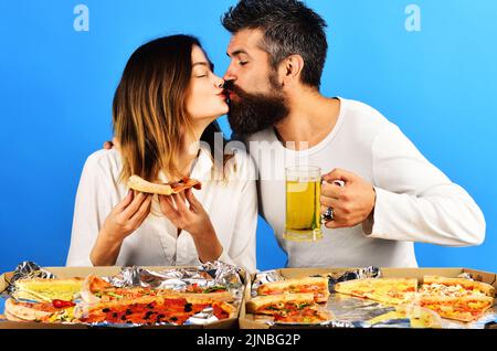 Ein Paar sitzt am Tisch und küsst Pizza. Frau mit Pizza in Scheiben und Mann mit einem Glas Bier. Stockfoto