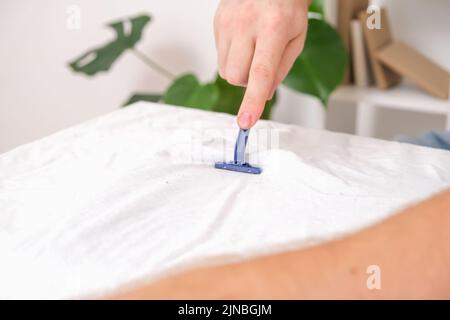 Ein Mann entfernt Stofftabletten mit einer Einweg-Rasiermaschine. Ein Rasiermesser zum Entfernen von Pellets. Stockfoto