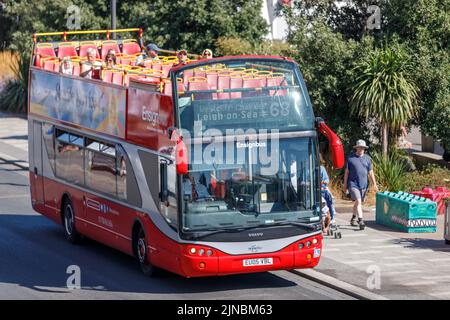 Red Bus mit offenem Oberdeck auf einer Besichtigungstour am Strand von Southend Beach, Marine Parade mit Passagier auf dem Oberdeck und Touristen, die auf dem Bürgersteig spazieren Stockfoto