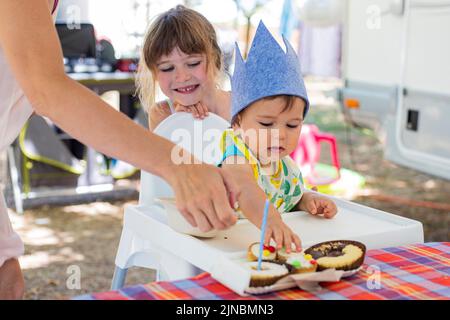 Kinder und Familie feiern die erste Geburtstagsparty des Jungen auf einem Campingplatz während der Sommerferien, außerhalb des Wohnwagens. Stockfoto