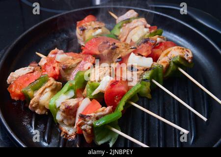 Leckere hausgemachte Fleisch- und Gemüsespieße, die auf einem schwarzen Grill gegrillt werden Stockfoto