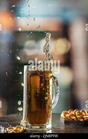 Glas mit leichtem kaltem Bier mit Spritzern und fliegenden Tropfen mit Snacks auf dem Tisch im Pub. Vertikale Ausrichtung Stockfoto