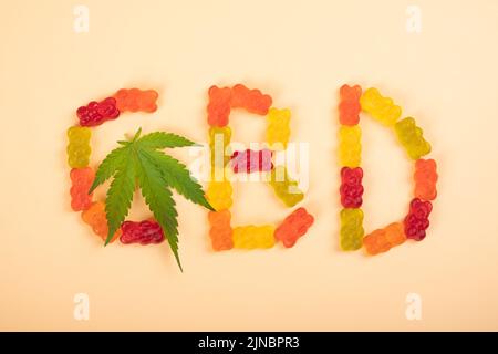 Farbige cbd-Süßigkeitengelee und Schrift mit Cannabis-grünen Blättern. Stockfoto