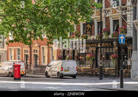 London, Großbritannien - 4. Juli 2022: Sherlock Holmes Pub in der Northumberland Street unter grünem Laub und Autos davor. Stockfoto