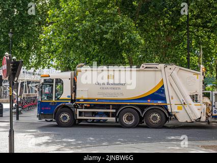 London, Großbritannien - 4. Juli 2022: Nahaufnahme des Müllwagens der Stadt White-blue Westminster, der unter grünem Laub geparkt ist. Reihen von Fahrrädern im Rücken. Stockfoto