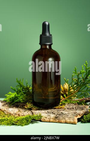 Glasflasche mit Körperöl. Konzeptionelle Zusammensetzung von ätherischem Öl, Moos und Baumrinde auf grünem Hintergrund. Oleum zur Haut- und Haarpflege. Stockfoto