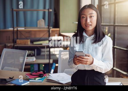 Junge asiatische Geschäftsfrau steht im Büro und hält Telefon Stockfoto
