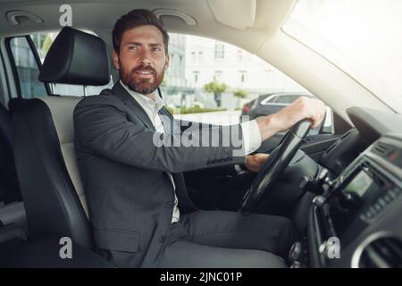 Ein gutaussehender Geschäftsmann in grauem Anzug fährt hinter dem Lenkrad des Autos Stockfoto