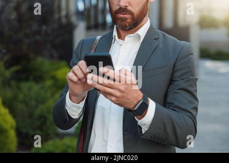 Nahaufnahme eines nicht erkennbaren Geschäftsmannes mit Telefon in der Nähe des Bürogebäudes Stockfoto