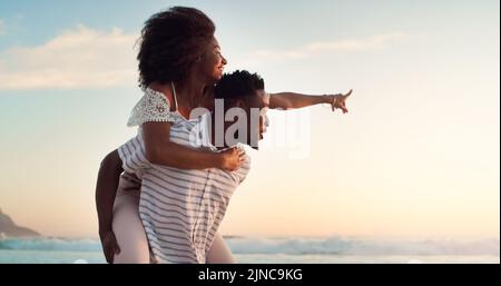 Eine fröhliche junge Frau, die von ihrem Freund am Strand mit Huckepack getragen wird. Stockfoto