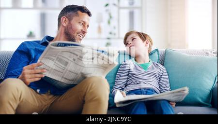 Er muss wissen, dass Wissen Macht ist. Ein hübscher Vater und Sohn lesen gemeinsam die Zeitung, während sie zu Hause auf einer Couch sitzen. Stockfoto