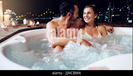 Wir feiern unseren Hochzeitstag mit Stil. Ein liebevolles reifes Paar, das sich nachts in einem Whirlpool entspannt. Stockfoto