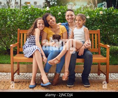 Tolle Zeit mit unserem Lieblingsmitglied der Familie. Porträt einer glücklichen Familie, die mit ihrem Hund auf einer Bank im Park spielt. Stockfoto