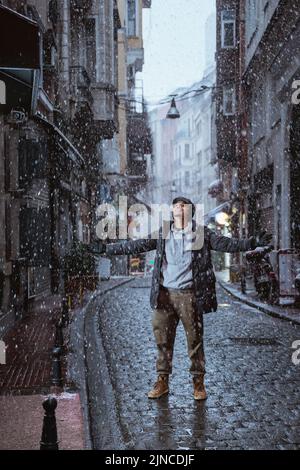 Mann, der mitten auf der Straße steht und den Schneefall genießt Stockfoto