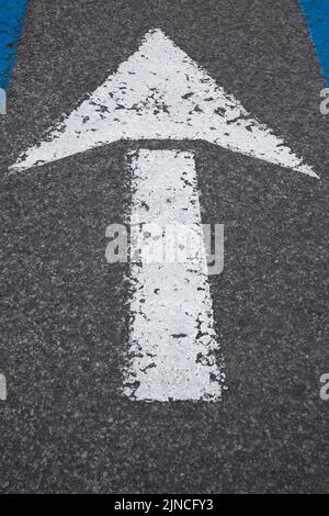 Weiß lackierter Autofahrtrichtungspfeil mit abblätternder Farbe auf schwarzem Asphaltpflaster. Stockfoto