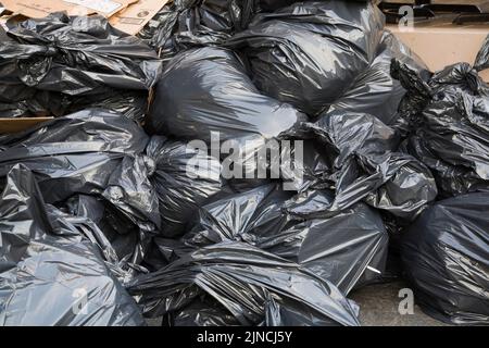 Schwarze Plastik-Müllsäcke und plattierte Kartons auf dem Bürgersteig der Stadt. Stockfoto