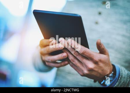 HES durchläuft vor dem Meeting schnell seine E-Mails. Ein nicht erkennbarer Geschäftsmann, der sein digitales Tablet bei der Arbeit nutzt. Stockfoto