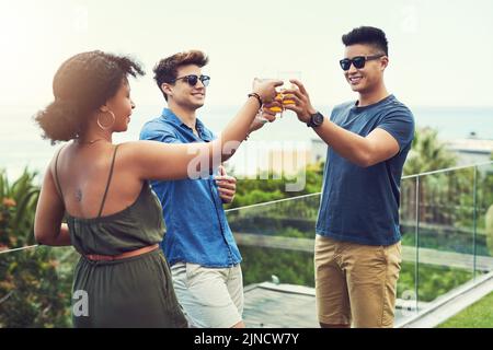 Toasting zu vielen weiteren Jahren der Freundschaft. Eine Gruppe von Freunden trinken und teilen sich einen Toast zusammen draußen während des Urlaubs. Stockfoto