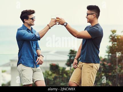 Heres to a lifetime of Friendship Buddy. Zwei schöne junge Männer mit Getränken und Entspannung im Freien während des Urlaubs. Stockfoto