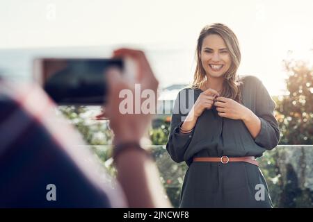 Meine eigene Schönheitskönigin. Eine attraktive junge Frau lacht, während ihr Freund Fotos von ihrer Außenterrasse macht. Stockfoto