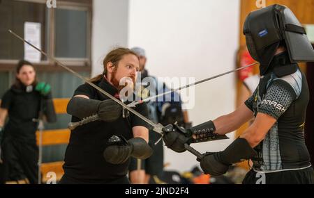 Ulm, Deutschland. 02. August 2022. Trainer Michael Hein (l.) demonstriert in der Jahnhalle in Schutzkleidung die Schwertkampftechniken eines Gegners. Diese Art von Fechten beinhaltet den Kampf mit langen Waffen. (To dpa 'das Duell der 'Schwäbischen Federn' - Schwertkampf als Hobby') Quelle: Stefan Puchner/dpa/Alamy Live News Stockfoto