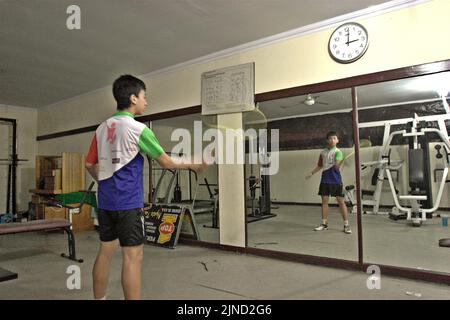 Im Jaya Raya Badmintonclub in Jakarta, Indonesien, übt ein junger Badmintonathlet verschiedene Schläge vor einem großen Spiegel. Stockfoto