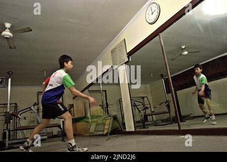 Im Jaya Raya Badmintonclub in Jakarta, Indonesien, übt ein junger Badmintonathlet verschiedene Schläge vor einem großen Spiegel. Stockfoto