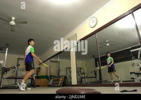 Im Jaya Raya Badmintonclub in Jakarta, Indonesien, übt ein junger Badmintonathlet verschiedene Schläge vor einem großen Spiegel. Stockfoto