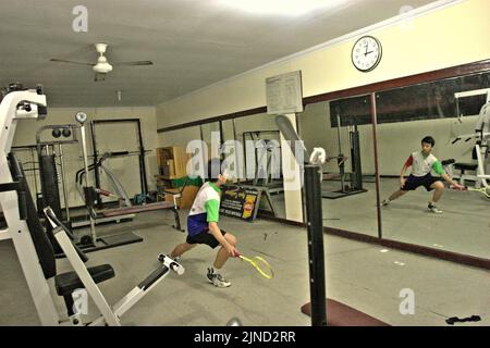 Im Jaya Raya Badmintonclub in Jakarta, Indonesien, übt ein junger Badmintonathlet verschiedene Schläge vor einem großen Spiegel. Stockfoto