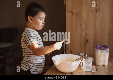 Kind saugt seinen Finger, um Schlagsahne zu probieren, macht und kocht in der Küche zu Hause. Für Lifestyle-Design. Köstlicher Geschmack. Stockfoto