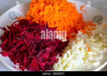 Gehackte Karotten, Zwiebeln und rote Rüben auf einem Teller aus der Nähe. Vorbereitung zum Kochen. Selektiver Fokus Stockfoto