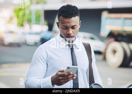 Technologie ermöglicht es ihm, durch den Betondschungel zu navigieren. Ein hübscher junger Geschäftsmann, der in der Stadt ein Handy benutzt. Stockfoto