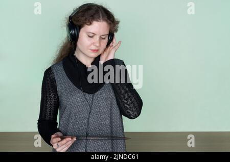 Junge Frau mit lockigen Haaren hört Musik mit Kopfhörern, die Vinylscheibe halten Stockfoto