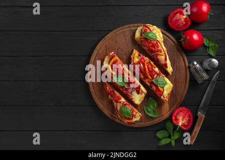 Glutenfreie Pizza Fladenbrot. Pizza auf Fladenbrot mit Gemüse auf schwarzem Holzboden. Die in Scheiben geschnittene Pizza liegt auf einem Holzständer. Stockfoto