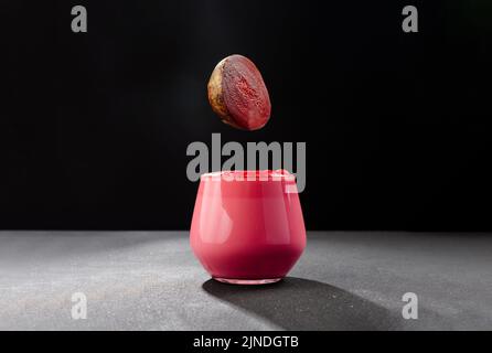 Eine Tasse Rüben-Latte auf dunklem Grund. Gesunde Ernährung Alternative zu Koffein. Eine rote Bete fällt in eine Tasse Kaffee. Stockfoto
