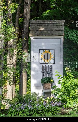 Altes Nebengebäude in einem Garten, das mit einem wunderschönen Quilt-Design und davor wachsenden Hostablumen dekoriert ist. Stockfoto