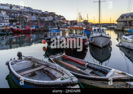 Blick auf die Uferpromenade bei Sonnenaufgang über den inneren Hafen von Mevagissey in Cornwall, mit dem kleinen Fischmarkt im Hintergrund. Stockfoto