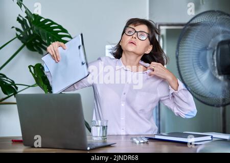 Frau mittleren Alters, die an Hitze leidet, überhitzt, durch Ventilator und Ventilator gekühlt Stockfoto