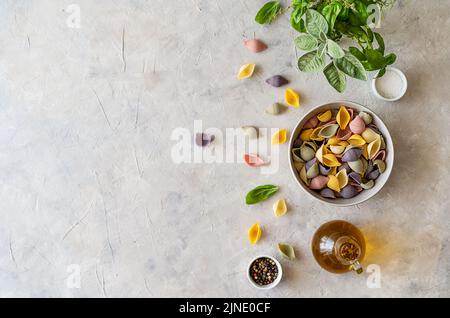 Mehrfarbige italienische Pasta Conchiglie oder Muscheln in Schüssel, Olivenöl, Gewürze, Kräuter. Flach mit Kopierplatz. Stockfoto