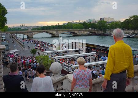 Zwei Paare gehen die Stufen hinunter, um sich der riesigen Menschenmenge anzuschließen, die an der seine hängt. Schöner Sommertag im Freien in Paris, Frankreich. Stockfoto