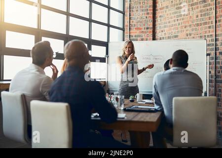 Selbstbewusst, Führung und Macht durch eine Geschäftsfrau, die eine Präsentation auf einem Brett vor einer Gruppe in einem Konferenzraum vorführt. Glückliche Frau erklärt eine Idee oder Stockfoto