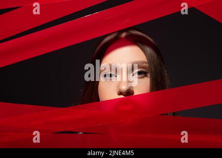 Teenage-Modell Blick auf die Kamera durch rote Streifen von Klebeband isoliert auf schwarz, recyceln Mode-Konzept Stockfoto