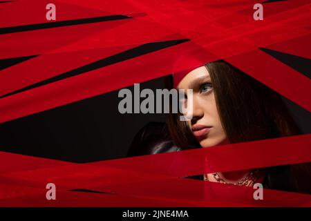 Teenager-Modell durch rote Streifen von Klebeband auf schwarzem isoliert, recyceln Mode-Konzept Stockfoto