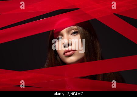 Teenage-Modell Blick auf die Kamera durch rote Streifen von Klebeband isoliert auf schwarz, recyceln Mode-Konzept Stockfoto