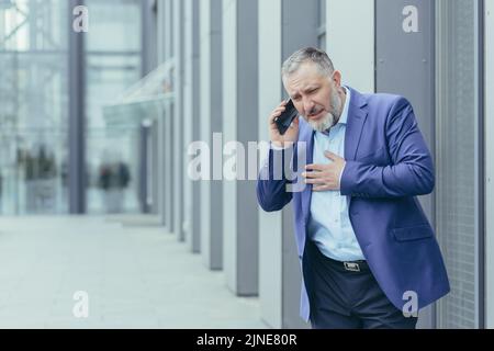 Leitender grauhaariger Mann im Geschäftsanzug hat starke Brustschmerzen, Herzinfarkt, Geschäftsmann ruft Arzt und Krankenwagen Stockfoto