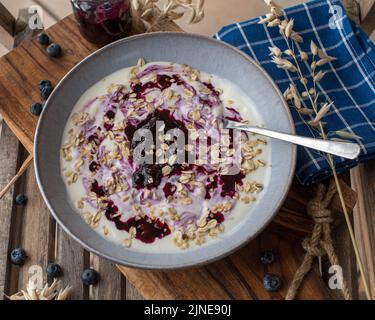 Frühstücksjoghurt mit Heidelbeerkompott und Haferflocken in einer Schüssel mit Löffel Stockfoto