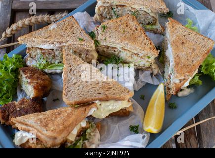 Fischkuchensandwiches mit Käse, Salat und Sauerrahm, Kräutersauce auf einem Tablett Stockfoto