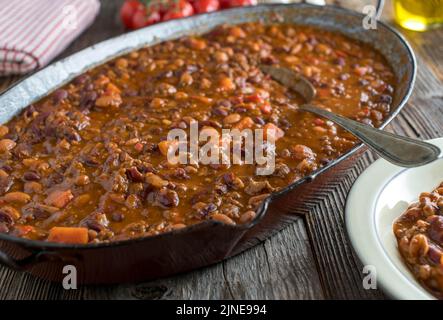 Hackfleisch mit Bohnen, Süßkartoffeln und Gemüse - Chili con Carne in einer altmodischen Bratpfanne auf einem Holztisch Stockfoto