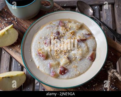 Haferbrei aus Hirse mit Äpfeln, Nüssen und Ahornsirup, serviert in einer altmodischen Emaillschüssel oder einem Teller mit Holzhintergrund Stockfoto