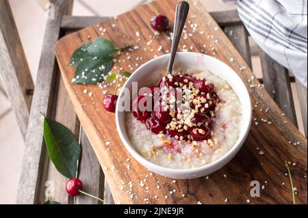 Haferbrei mit saurer Kirschkompott auf Holzhintergrund Stockfoto